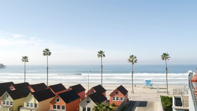 Colorful waterfront cottages, Oceanside California USA. Multicolor bungalow huts, summer sea, beachfront lodging. Many vacation houses on beach, ocean waves and palm trees. Lifeguard tower, watchtower