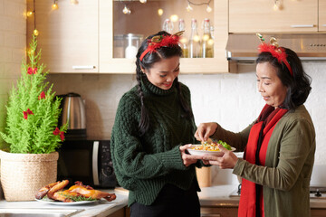 Senior woman explaining adult daughter how to garnish salad with greenery before bringing to...