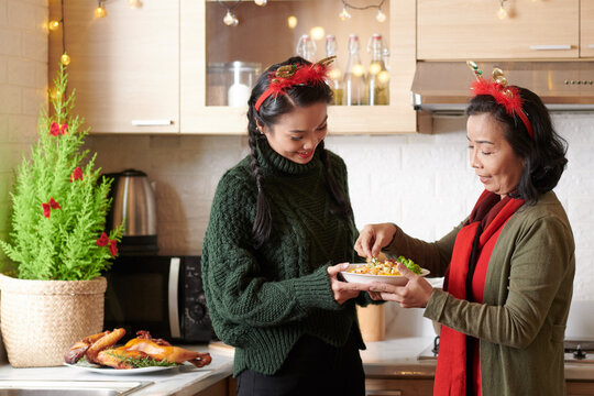 Senior woman explaining adult daughter how to garnish salad with greenery before bringing to Christmas dinner table