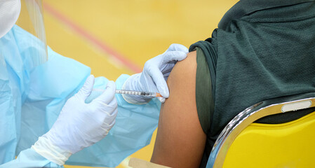 Close-up and selective focus of doctor hands who is vaccinating on upper arm of young man for build...