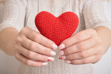 Fototapeta premium A red knitted heart in the hands of a girl with a beautiful manicure. Love. Organ donation.