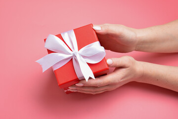 Top view a woman's hand holds a pink gift box with a white ribbon on a blue background.