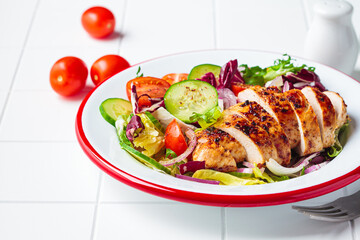 Chicken breast salad with cucumber, tomato and onion in a white plate, white background.