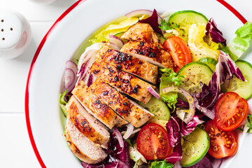 Chicken breast salad with cucumber, tomato and onion in a white plate, white background.