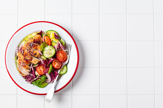 Chicken breast salad with cucumber, tomato and onion in a white plate, white background.