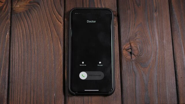 Close-up of an incoming call from a doctor on a mobile phone screen on a brown wooden background.