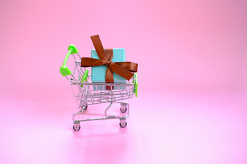 A present box with a ribbon in a shopping trolley cart on pink background . Concept - buying a gift...