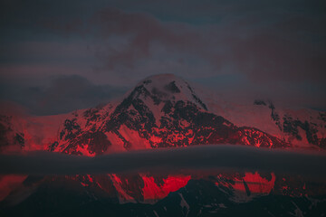 Surreal mountain landscape with great snowy mountains lit by dawn sun among low clouds. Fantasy...