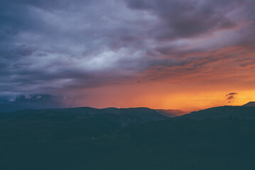 Atmospheric landscape with silhouettes of mountains with trees on background of vivid orange blue violet dawn sky. Colorful nature scenery with sunset or sunrise of illuminating color. Sundown paysage