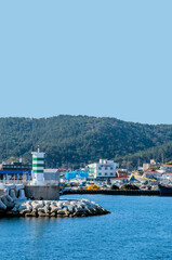 Landscape of small seaport with green and white lighthouse on pier.