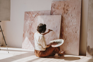 Young woman artist painting abstract picture in studio with sun light. Aesthetic minimalist art...