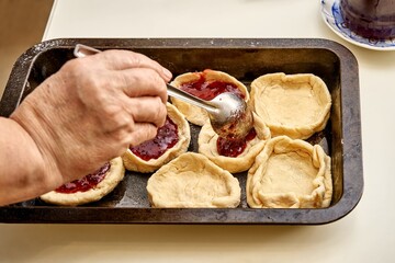 Senior woman fills raw pies with natural homemade berry jam cooking dessert at white table in...