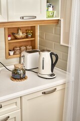 Stylish teapot with freshly brewed hot drink near electric kettle and toaster on white countertop in elegant kitchen interior - 475971702