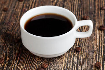 a white mug with a black drink and coffee beans