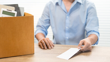 Resignation Concept The male officer sitting, putting his box of his belongs on the desk and handing the white letter to someone