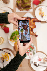 Hands of woman photographing Christmas dinner table she served for family celebration