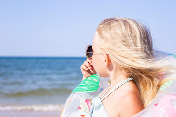 Child girl with sunglasses with a rubber ring on the beach.