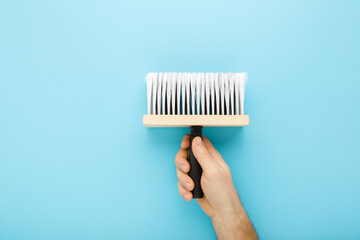 Naklejka premium Young adult man hand holding new brush on light blue table background. Pastel color. Closeup. Preparation for repair work of home. Top down view.
