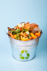 Sorted kitchen waste in compost-bucket on blue background. Compost-container front view. Sustainable lifestyle. Vegetable, fruit peels, scrap from food preparation collected in trash-can for recycling