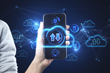 Close up of hand holding smartphone with abstract glowing cloud computing hologram with download/upload arrows on blurry blue city background. Database, technology and future concept. Double exposure.