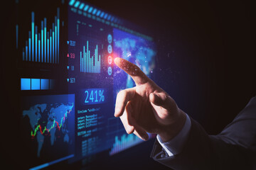 Close up of businessman hand pointing at abstract glowing blue business forex chart and map interface on dark backdrop. Trade, finance, analysis, growth, technology and innovation concept.