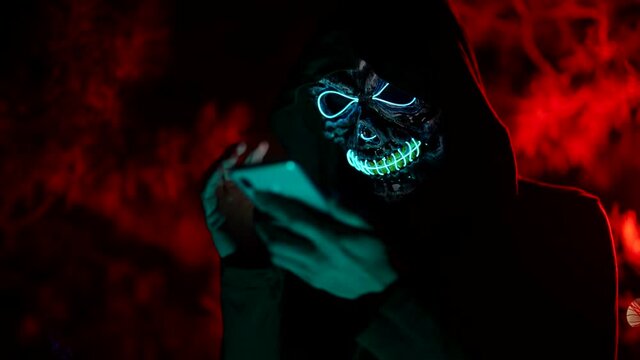 mysterious person with glowing mask of skull is using smartphone, agressive anonymous comments