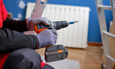 Craftsman holding a screwdriver drill ready to perform home renovation. Worker in work clothes on a construction site on an aluminum folding ladder in an apartment.