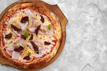 pizza with veal, ham, cheese and sun-dried tomatoes on a gray table