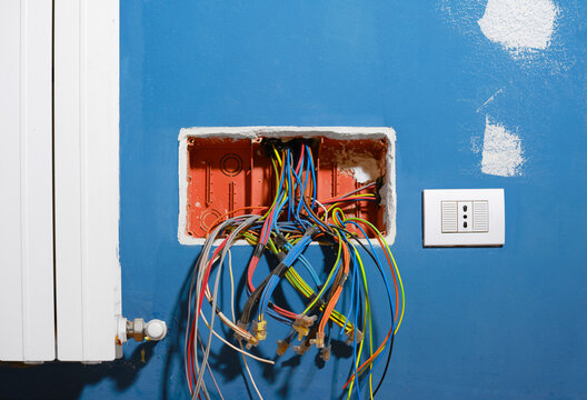 Colored Electrical Cables Coming Out Of An Open Junction Box, During The Renovation Of An Apartment. Electrical Cables Coming Out Of The Corrugated Pipes Inside The Junction Box Located In A Blue Wall