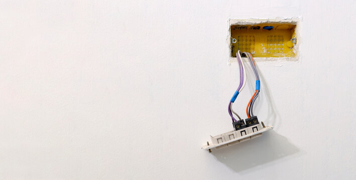 Colored Electrical Cables Coming Out Of A Corrugated Tube Of An Electrical Box, From A White Wall, In An Apartment Under Renovation. Buttons And Switches Of A Wall Mounted Electrical Box.