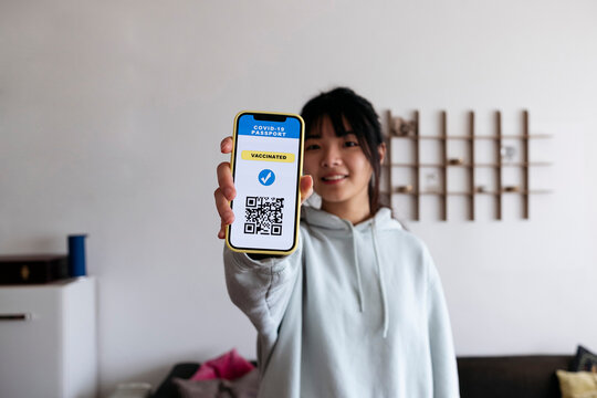 Young woman holding mobile phone with vaccination QR code on screen