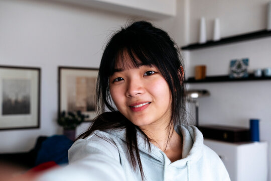 Smiling woman with bangs taking selfie at home