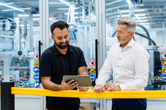Businessmen using tablet PC at railing in factory