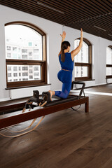 Young girl doing pilates exercises with a reformer bed. Beautiful slim fitness trainer on reformer. Fitness concept