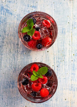 Two glasses of gin tonic with mint, ice cubes and raw berries