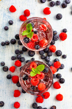 Two glasses of gin tonic with mint, ice cubes and raw berries