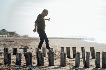 Senior man balancing on wooden posts at beach