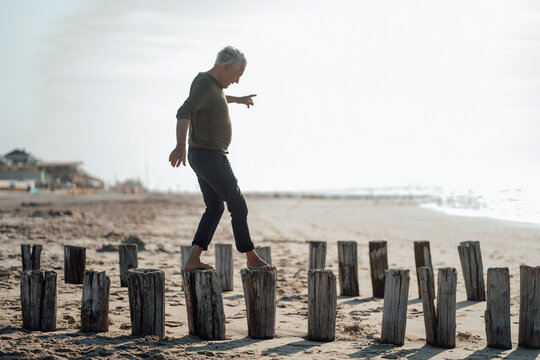 Senior man balancing on wooden posts at beach