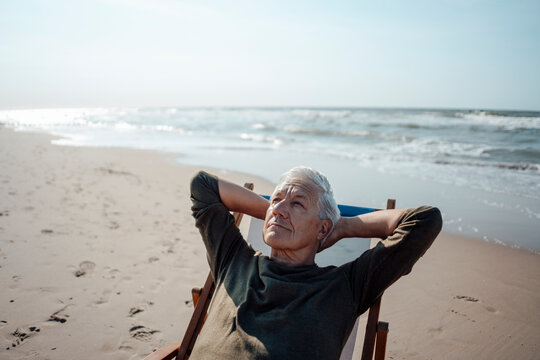 Senior man looking up relaxing on chair at beach