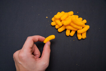 Top view of a person taking a cheese puff on a black surface - obrazy, fototapety, plakaty