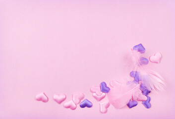 Feathers and pink and purple satin hearts in a cornar arrangement on paper texture for Valentine Day