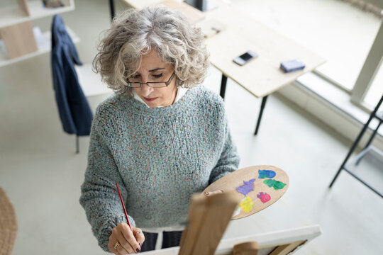 Concentrated senior woman painting on canvas at home