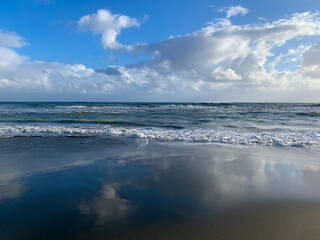 Seascape, white clouds on the blue sky reflection, sea surface, sand beach