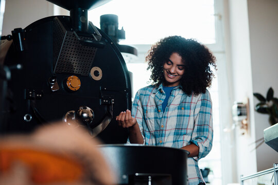 Smiling owner roasting coffee beans in machine at roastery