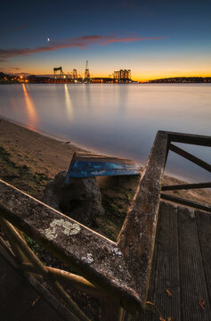 Spain, Province of A Coruna, Fene, Weathered coastal railing at dusk with town harbor in background