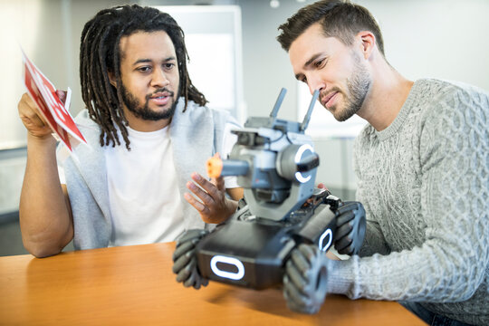 Engineers discussing with each other looking at robotic combat tank in workshop