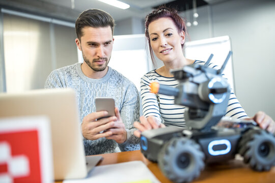Engineer checking robotic combat tank with colleague at workshop