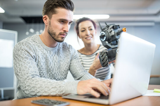Technician checking programming of robotic car held by colleague at workshop