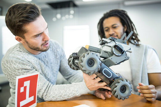 Engineer looking at robotic combat tank with colleague at workshop