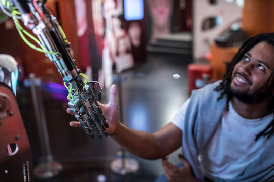 Young tech developer shaking hand with robotic arm at workshop